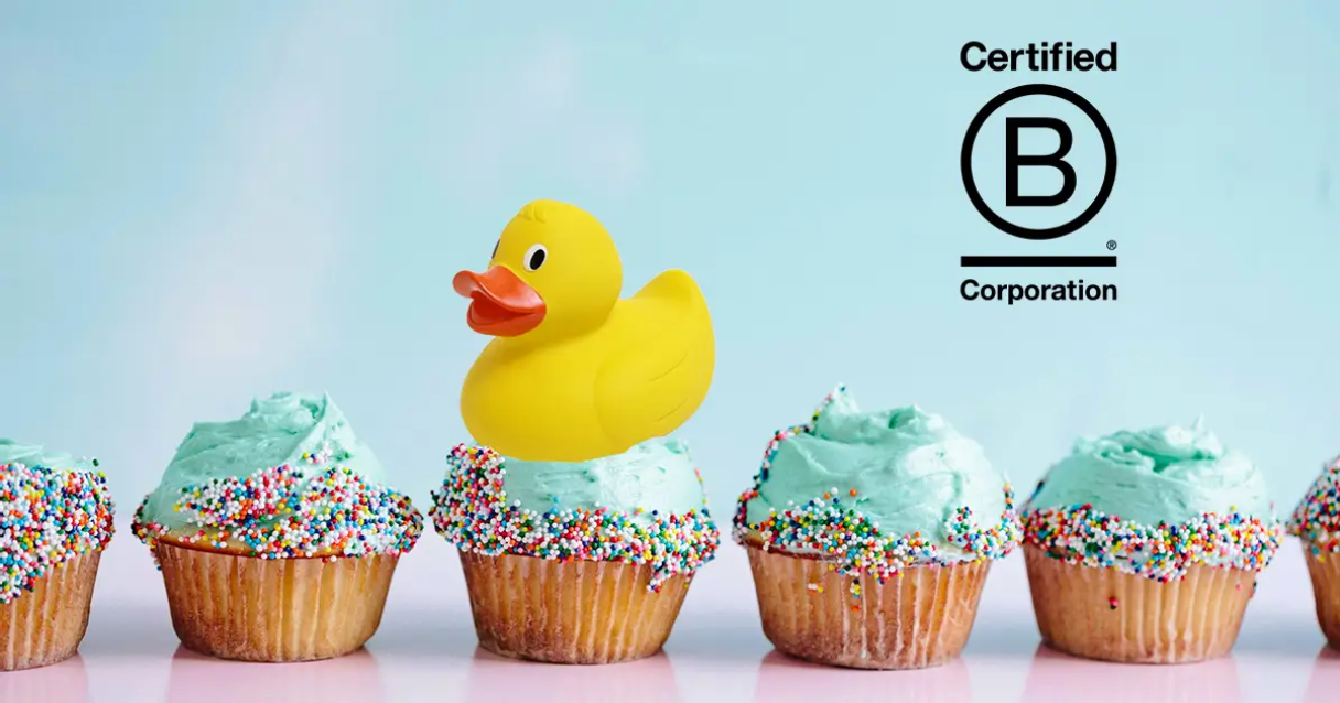 A rubber duck sits on top of a cupcake in a row of cupcakes with the B Corp logo above them